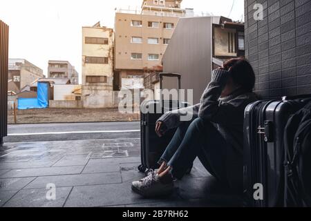 Eine Frau, die mit einem Gefühl traurig sitzt, während sie mit vielen Baggages auf dem Boden unterwegs ist Stockfoto