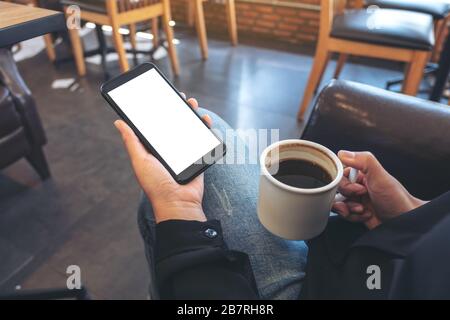 Verspottes Bild von Händen, die weißes Handy mit leerem Bildschirm halten, während sie Kaffee in einem modernen Café trinken Stockfoto