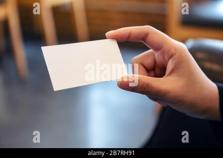 Eine Hand, die weiße leere Visitenkarte mit verschwommenem Hintergrund enthält Stockfoto