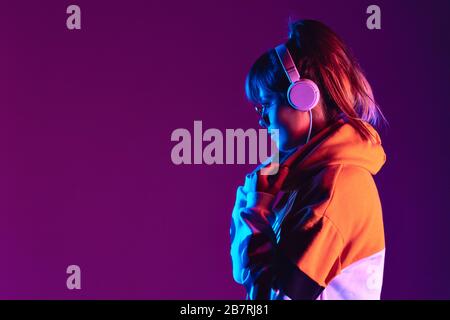 Happy Girl mit modischer Brille Kopfhörer hören Sie Musik im violetten Hintergrund. Stockfoto
