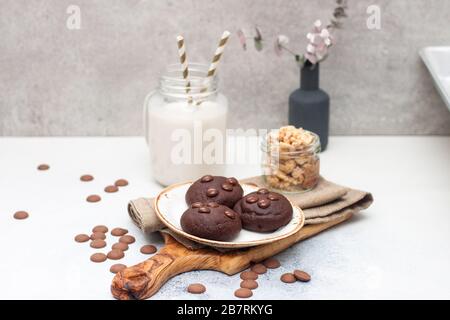 Schokoladenplätzchen mit Choco-Tropfen auf weißem Teller und Glas auf grauem Hintergrund Stockfoto