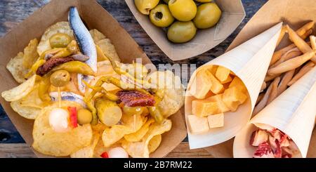 Tapas und Pinchos Panoramaaufnahme über dem Kopf. Käse, Jamon und Oliven, gildas und Sardinen auf einem Holztisch in einem Café im Freien Stockfoto