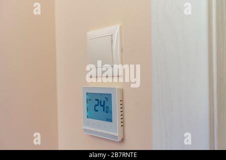 An der Wand des Raumes befindet sich ein Lichtschalter und darunter ein Fußbodenheizungsschalter mit einem Temperaturregler. Stockfoto