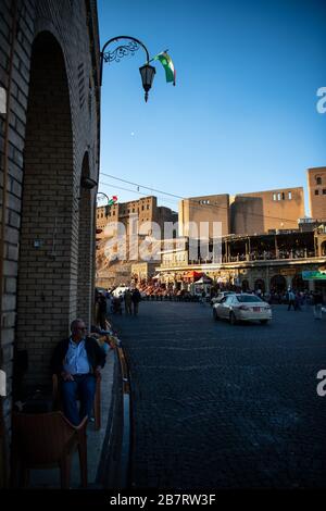 Irak, Iraq Kurdistan, Arbil, Erbil. Im Hintergrund steht die Zitadelle Erbil Qalat bei Sonnenuntergang, rechts fahren Taxis an der Straße ont He vorbei. Stockfoto