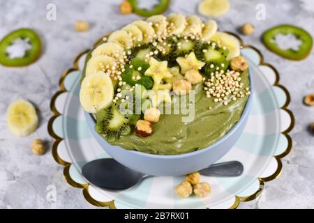 Smoothie-Schüssel aus grünem Obst mit sternförmigen Bananen, Kiwi, Haselnuss und gebucktem Quinoa-Korn auf grauem Grund Stockfoto