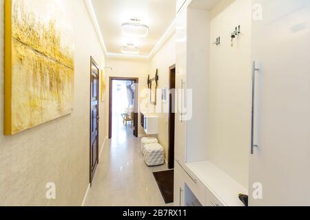 Ein langer Korridor in der Wohnung mit beigefarbenem Wallpaper, zahlreichen Türen und hellgelben abstrakten Malereien an den Wänden. Stockfoto