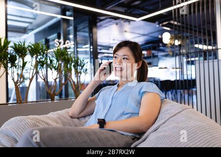 Asiatische Frau, die einen Telefonanruf in einer Bohnentasche hat Stockfoto