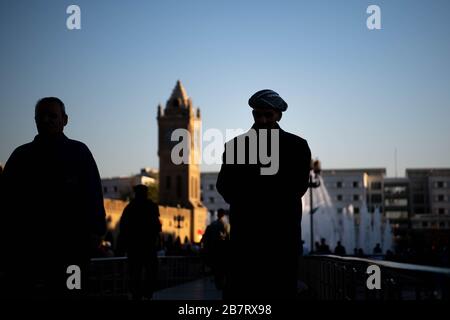 Irak, Iraq Kurdistan, Arbil, Erbil. Auf dem Park Shar laufen Silhouetten von Männern. Im Hintergrund steht Erbil Uhr und ein Brunnen Stockfoto