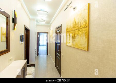 Ein langer Korridor in der Wohnung mit beigefarbenem Wallpaper, zahlreichen Türen und hellgelben abstrakten Malereien an den Wänden. Stockfoto