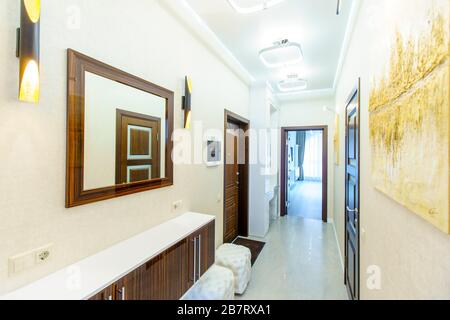 Ein langer Korridor in der Wohnung mit beigefarbenem Wallpaper, zahlreichen Türen und hellgelben abstrakten Malereien an den Wänden. Stockfoto