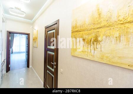 Ein langer Korridor in der Wohnung mit beigefarbenem Wallpaper, zahlreichen Türen und hellgelben abstrakten Malereien an den Wänden. Stockfoto
