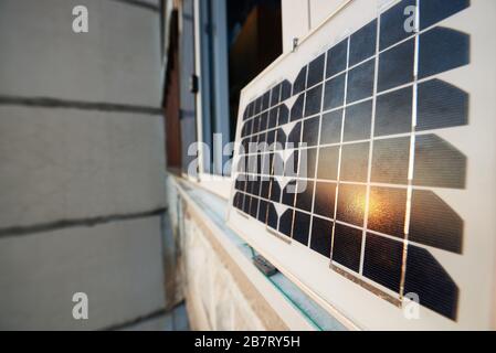Nahaufnahme eines Solarpanels, das auf einem Fenster eines Hochhauses steht und die Sonne bei Sonnenuntergang reflektiert. Konzept zur Umwandlung von Sonneneinstrahlung in Elektrizität Stockfoto