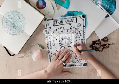 Draufsicht der Geburtskarte des Astrologen nach Kristallen und Aquarellzeichnungen auf Karten auf dem Tisch Stockfoto