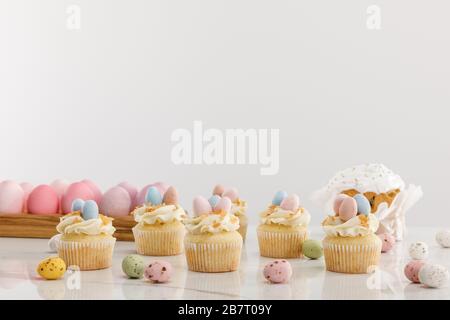 Köstliche Cupcakes mit bunt bemaltem Huhn und Wachteleiern in der Nähe von osterkuchen isoliert auf Grau Stockfoto