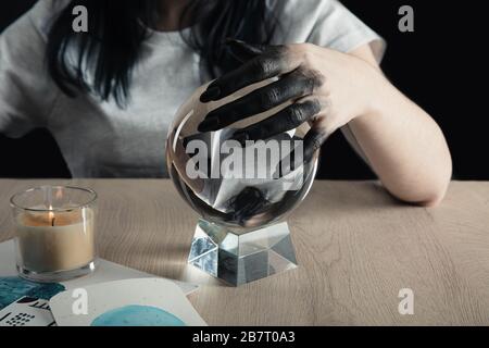 Beschnittener Blick auf den Zauberer mit schwarz lackierter Hand, die Kristallkugel durch Aquarellbilder und Kerze auf dem Tisch hält, isoliert auf Schwarz Stockfoto