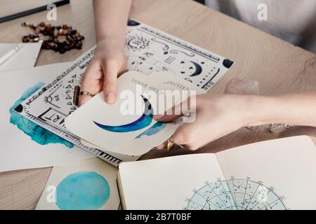 Beschnittener Blick auf die Astrologer-Haltekarten mit Aquarellzeichnungen nach Geburtskarte mit Tierkreiszeichen auf dem Tisch Stockfoto