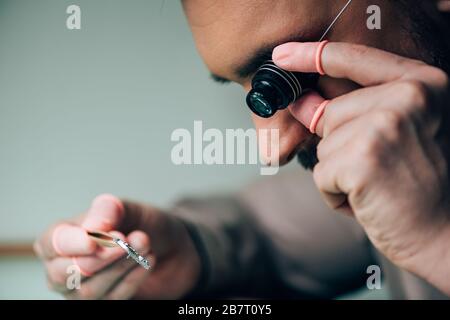 Seitenansicht des Uhrmachers mit Latex-Fingerspitzen, die Brillenlupe und Uhrenteil halten Stockfoto