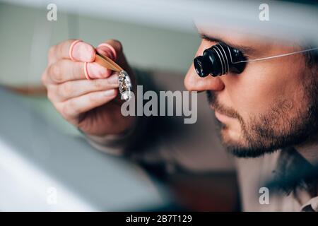 Seitenansicht des gutaussehenden Uhrmachers in Brillenlupe mit Blick auf Armbanduhrteil Stockfoto