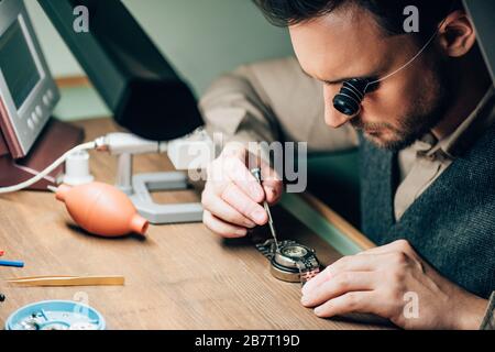 Seitenansicht des Uhrmachers in Brillenlupe Arbeiten mit Armbanduhr durch Ausrüstung auf dem Tisch Stockfoto