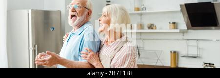 Panoramaaufnahme des älteren Paares, das lacht und Mann hält Pilze in der Küche Stockfoto