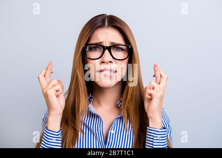 Junge süße Mädchen in formeller Kleidung und Brille halten die Finger gequodet, hoffen auf viel Glück, bevor sie zum Bewerbungsgespräch oder zur Prüfung gehen und die Lippe beißen Stockfoto