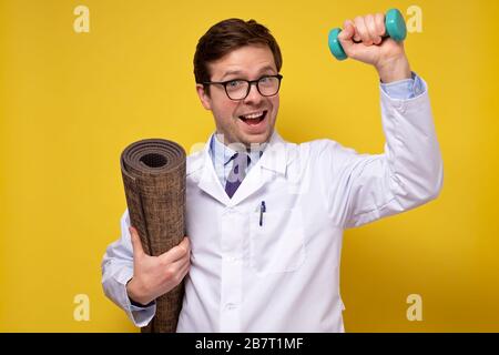Ein reifer kaukasischer Mannarzt, der Hanteln hält und Ratschläge zu einem gesunden Lebensstil gibt. Sport- und Medizinkonzept. Stockfoto