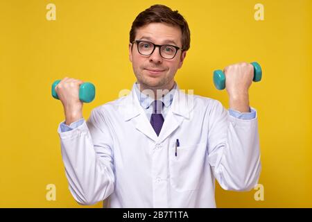 Ein reifer kaukasischer Mannarzt, der Hanteln hält und Ratschläge zu einem gesunden Lebensstil gibt. Sport- und Medizinkonzept. Stockfoto