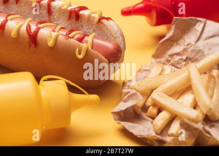 Leckerer heißer Hund, pommes frites in Papier und Flaschen mit Ketchup und Senf auf Gelb Stockfoto