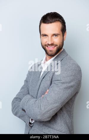Vertikales Foto eines lächelnden fröhlichen Unternehmers, der mit gekreuzten Händen auf grauem Hintergrund steht Stockfoto