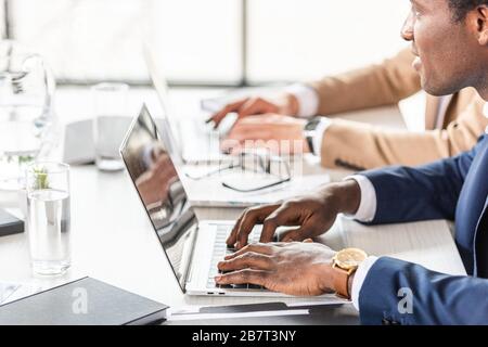 Teilansicht von zwei multiethnischen Geschäftsleuten, die Laptops am Tisch im Büro verwenden Stockfoto