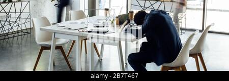 Panoramaaufnahme eines afroamerikanischen Geschäftsmannes, der auf dem Tisch im Büro schläft Stockfoto