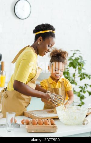Fröhliche afroamerikanische Mutter und Tochter kneten Teig auf dem Schneidebrett Stockfoto