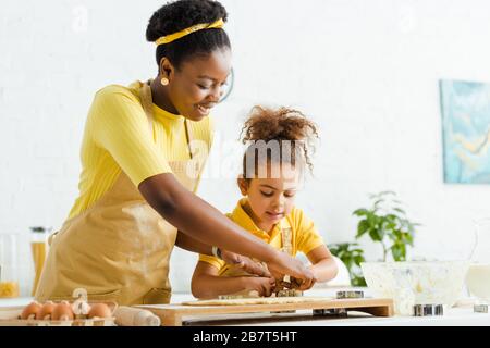 Glückliche afroamerikanische Mutter und Tochter, die Plätzchenschneider in der Nähe von Teig hält Stockfoto