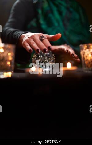 Fortuneteller Weissling auf Zauberkugel am Tisch mit brennenden Kerzen im dunklen Raum Stockfoto
