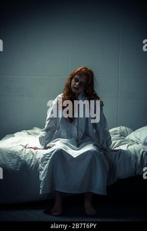 Creepy dämoniakale Frau in Nachtgown, die auf dem Bett sitzt Stockfoto