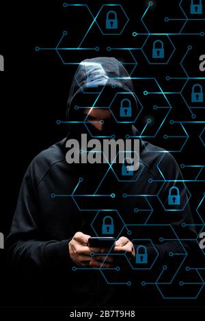 Hacker in der Haube, die Smartphone in der Nähe von Vorhängeschlössern auf schwarzem, Cyber-Sicherheitskonzept verwenden Stockfoto