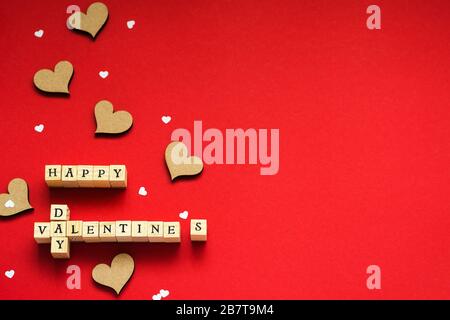 Schriftzug aus Holzwürfeln mit Buchstaben fröhlicher Valentinstag mit Herzen auf rotem Hintergrund Stockfoto