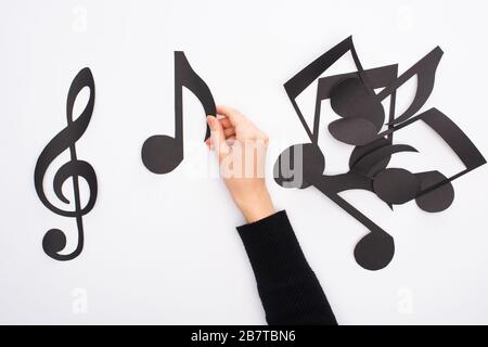 Beschnittene Ansicht der weiblichen Hand mit Papier, die schwarze Musiknoten auf weißem Hintergrund schneidet Stockfoto