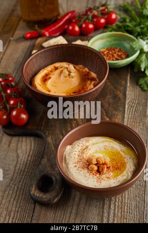 Selektiver Schwerpunkt von Schalen mit Paprika und Hummus, Gemüse und Petersilie auf Holzhintergrund Stockfoto