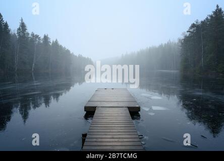 Nebelige Landschaft mit ruhigem See und Pier. Nebel über Wasser. Nebelige Luft. Frühkindlicher Morgen im Herbst. Schöner Freiheitsmoment und friedliche Atmosphäre Stockfoto