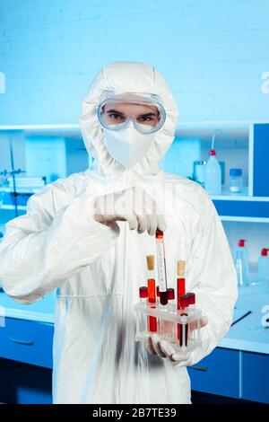 Wissenschaftler im Hazmatanzug und Latexhandschuhe mit Reagenzglas mit Schriftzug Stockfoto