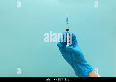 Hand in blaue Handschuhe, die Spritze isoliert auf blauem Hintergrund halten Stockfoto