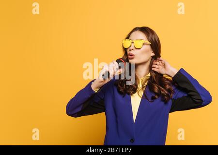 Schöner Sänger in gelber Brille mit Mikrofon auf gelbem Hintergrund Stockfoto