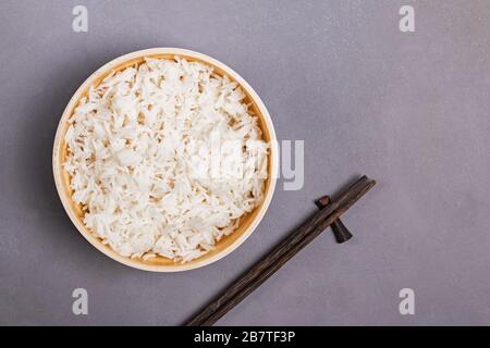 Schüssel mit gekochtem Jasminreis und Essstäbchen auf grauem Tisch Stockfoto