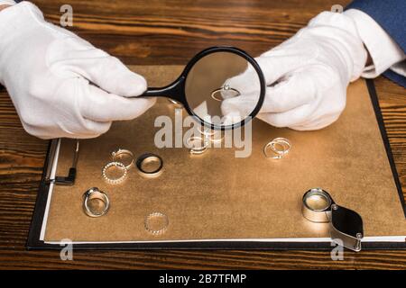 Beschnittener Blick auf den Juwelierschätzer, der Schmuckring und Lupe in der Nähe der Tafel auf dem Tisch hält Stockfoto