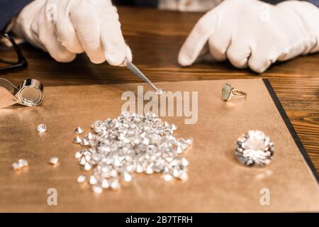 Beschnittener Blick auf den Schmuckschätzer, der Edelstein in Pinzetten in der Nähe der Tafel auf dem Tisch hält Stockfoto