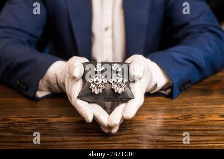 3/4-Ansicht des Juwelierschätzers, der Schmuckkissen mit Ohrringen am Tisch hält, isoliert auf Schwarz Stockfoto