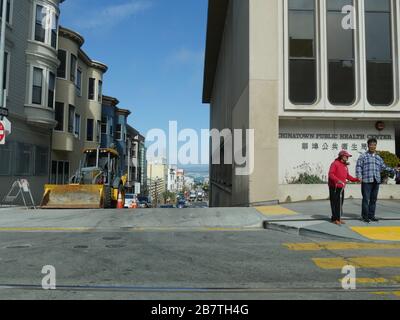 San Francisco, Kalifornien - Juli 2018: Zwei Menschen warten auf die Bordsteinkante, um die Straße vor dem Chinatown Public Health Center in San Francisco zu überqueren. Stockfoto