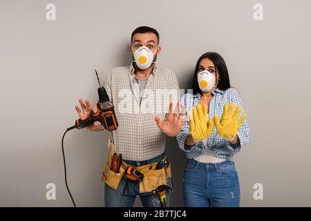 Verängstigte Handarbeiter in Sicherheitsmasken, die elektrische Bohrmaschine in Grau halten Stockfoto