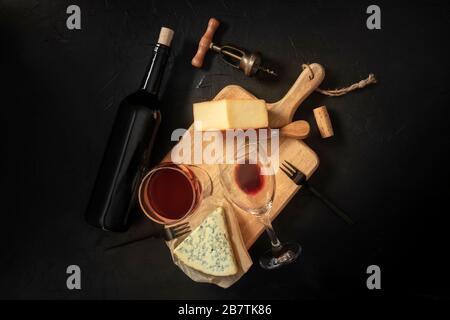 Wein- und Käseverkostung, oben auf schwarzem Hintergrund mit Kork, Korkenzieher und einer Flasche Stockfoto